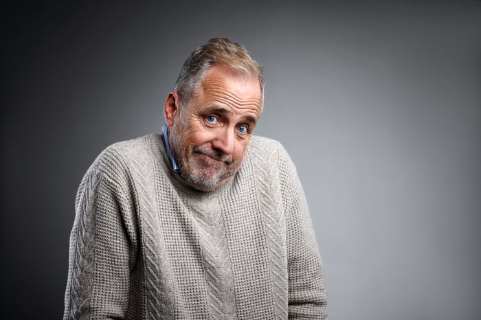 An elderly man shrugging his shoulders while smirking. 