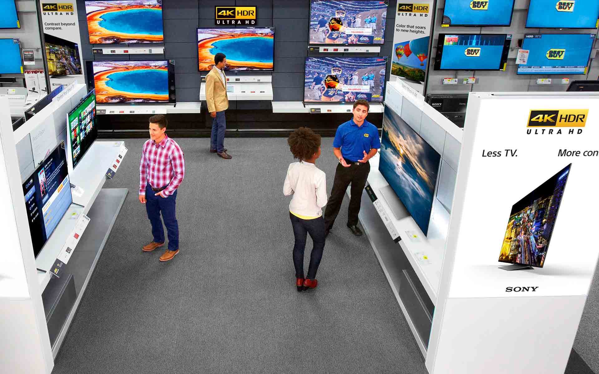 Best Buy televisions at the store with customers talking to a Best Buy salesperson.