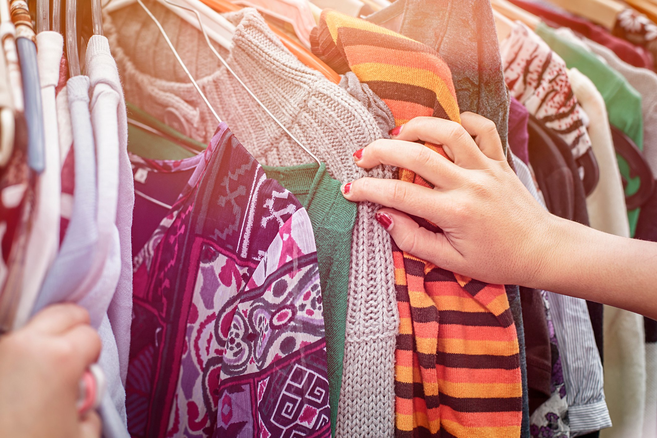 A woman's hand leafs through a rack of clothes.