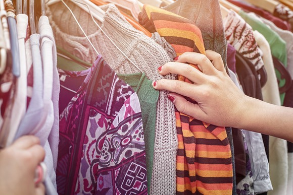 A woman's hand leafs through a rack of clothes.