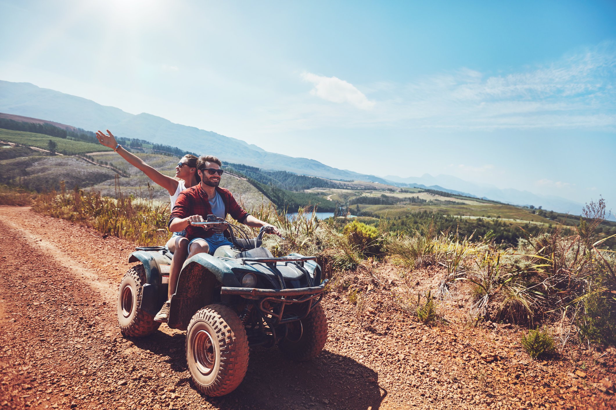 Off-road vehicle on a mountain road, with a man driving and a woman riding on back. 