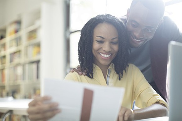 Couple smiling while they stare at paper, in library.