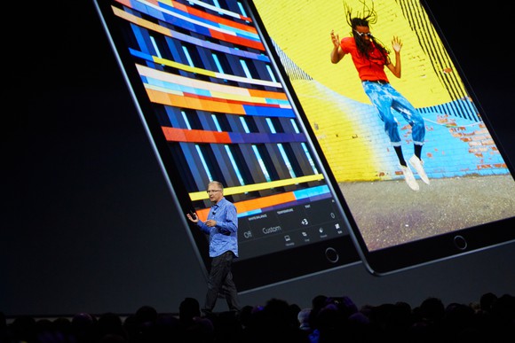 Apple executive Greg Joswiak on stage with images of the 10.5-inch iPad Pro projected on the screen behind him.