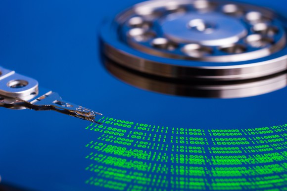 Close-up shot of a bare hard drive platter, where the read-and-write head is leaving green data traces on the black disk.