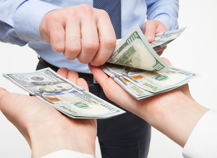 A businessman placing hundred dollar bills into the outstretched hands of another person. 