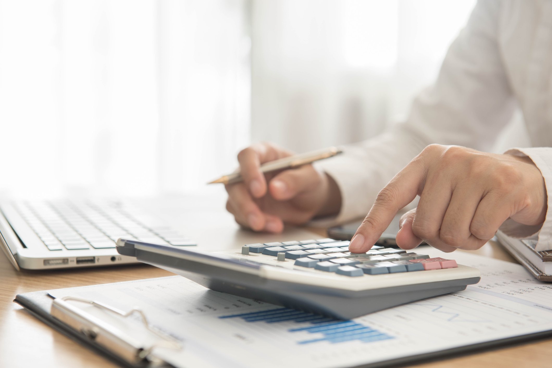 A person holding a pen with one hand, pressing buttons on a calculator with the other.