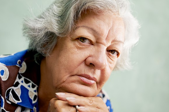 A senior woman in deep thought, with her head resting on her hands. 