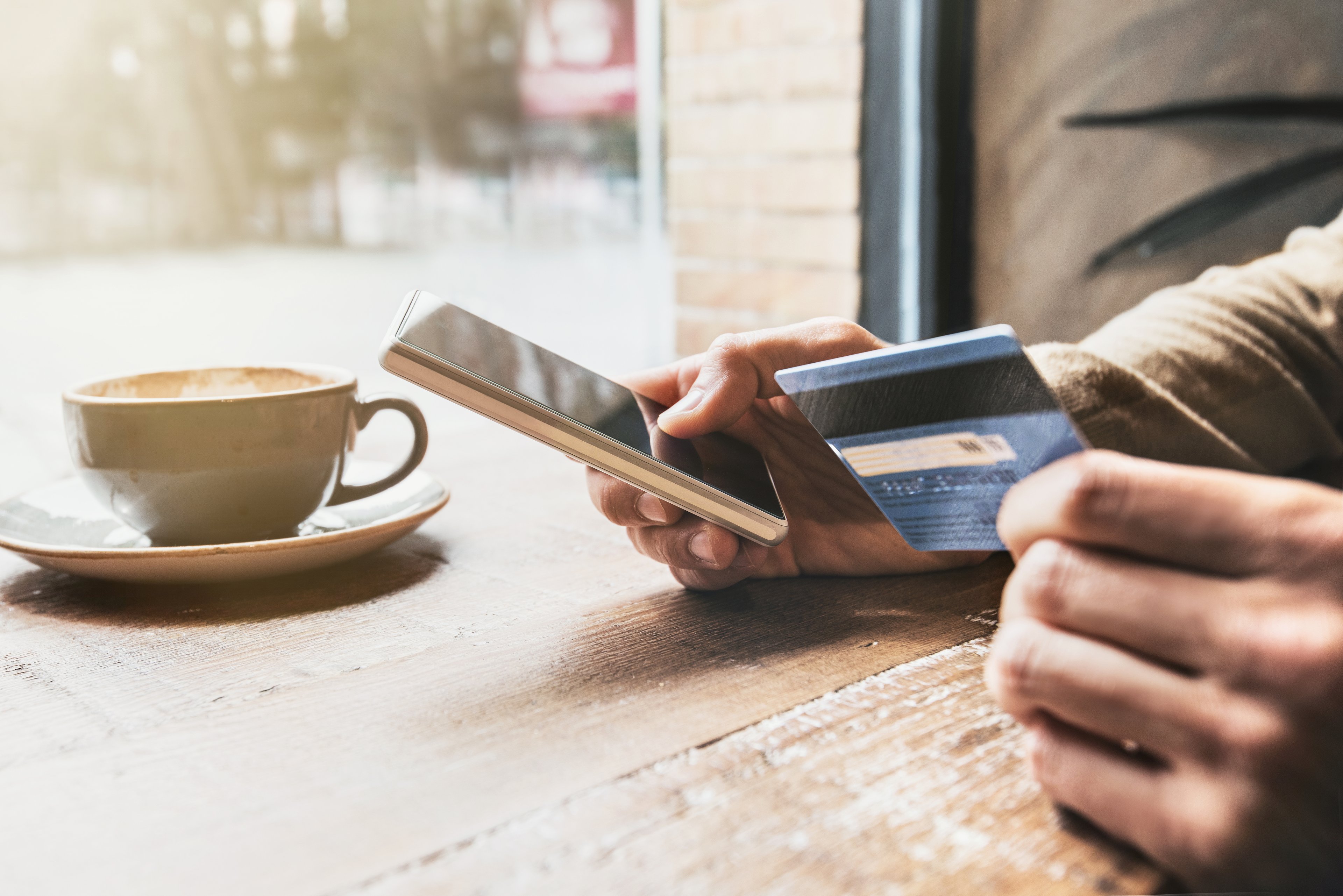 Person holding a credit card and a smartphone while sipping a latte.