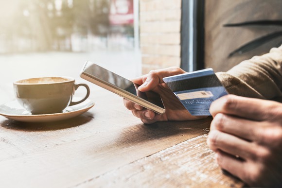 Person holding a credit card and a smartphone while sipping a latte.