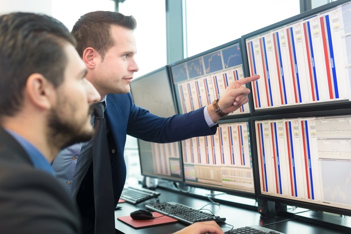 Two  businessmen looking at an array of monitors. 