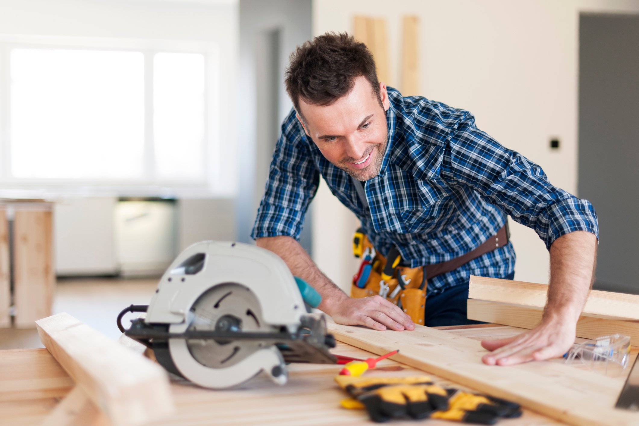 Handyman with tool belt working with wood using circular saw.