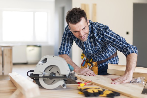 Handyman with tool belt working with wood using circular saw.