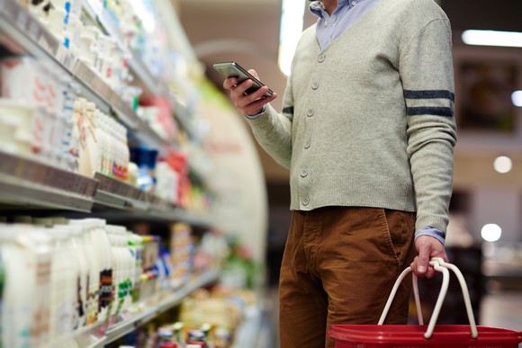 Man grocery shopping while looking at his smartphone.
