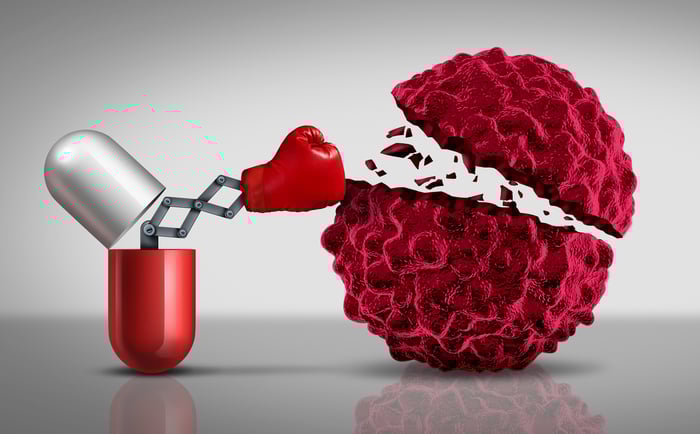 A capsule opening up to reveal a boxing glove that punches a cancer cell into two pieces. 