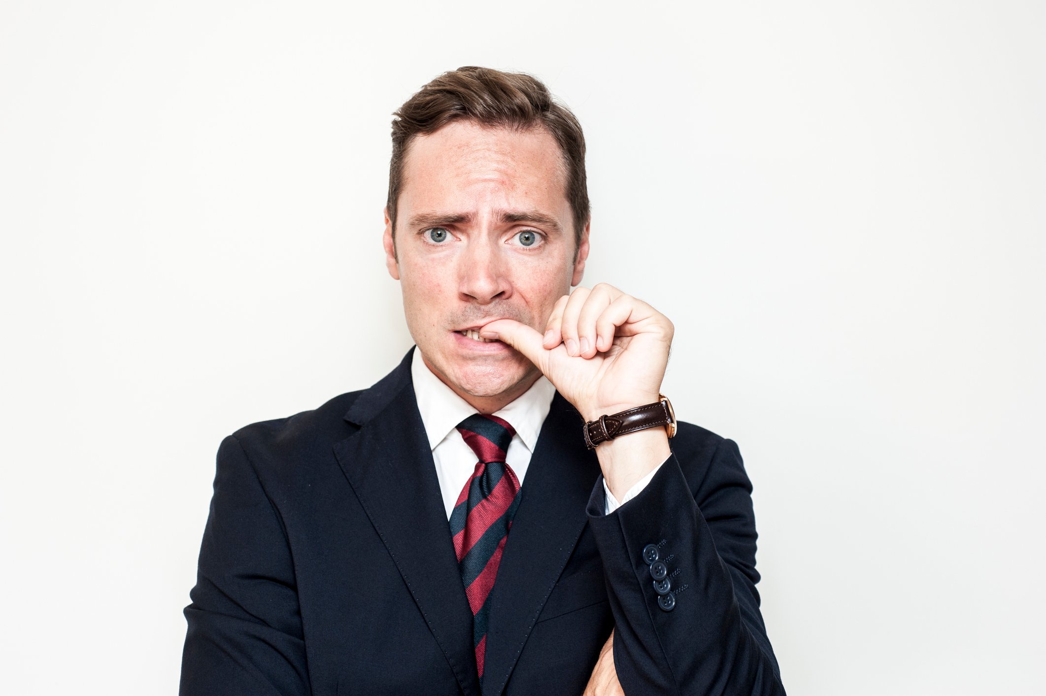 Man in a suit biting his thumbnail with a worried expression.