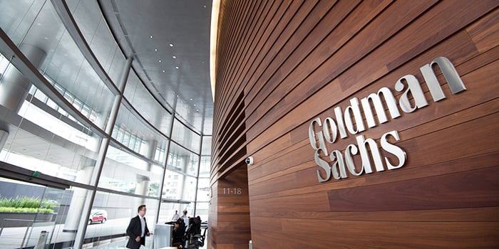 Lobby of a Goldman Sachs building, with glass outer walls and wood inner wall with company logo on it.