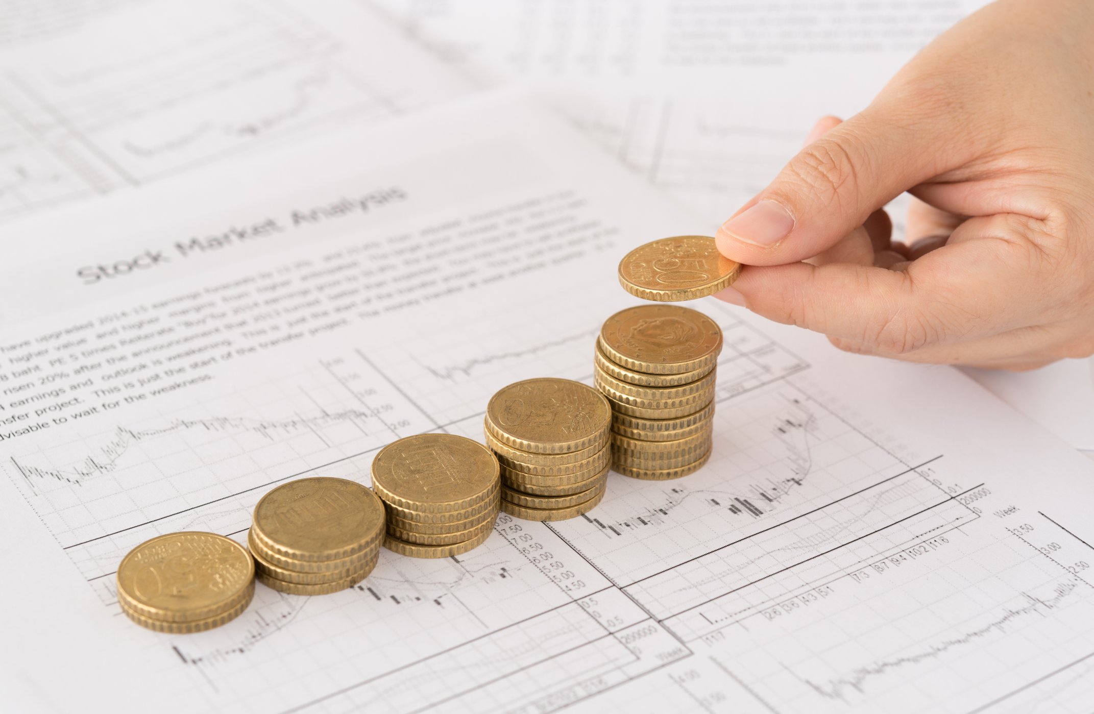 Five stacks of coins, ascending in size from right to left with a hand placing a coin on the last stack on the right.