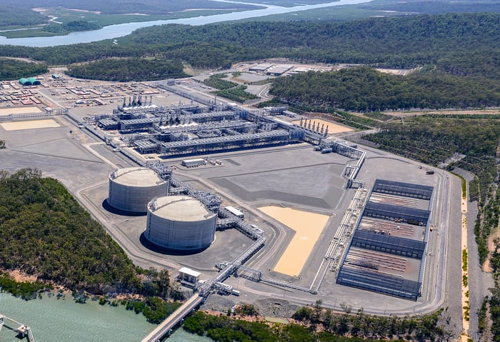 Energy facility with storage tanks surrounded by forest and a river.