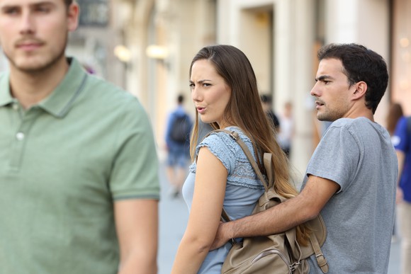 Woman walking with her boyfriend turns around to look at another man.