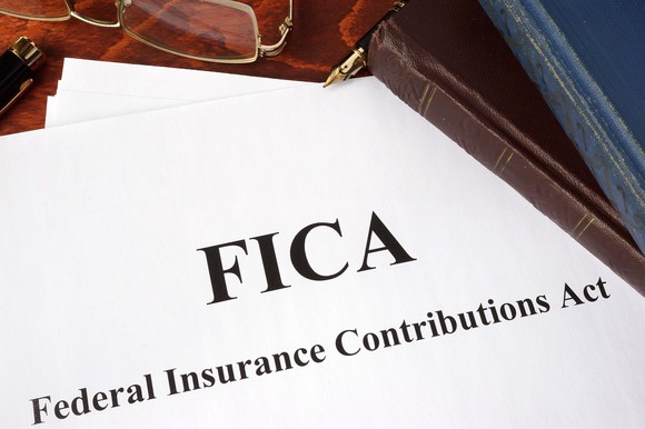 Paper saying FICA and what it means, along with glasses and books on a wood desk.