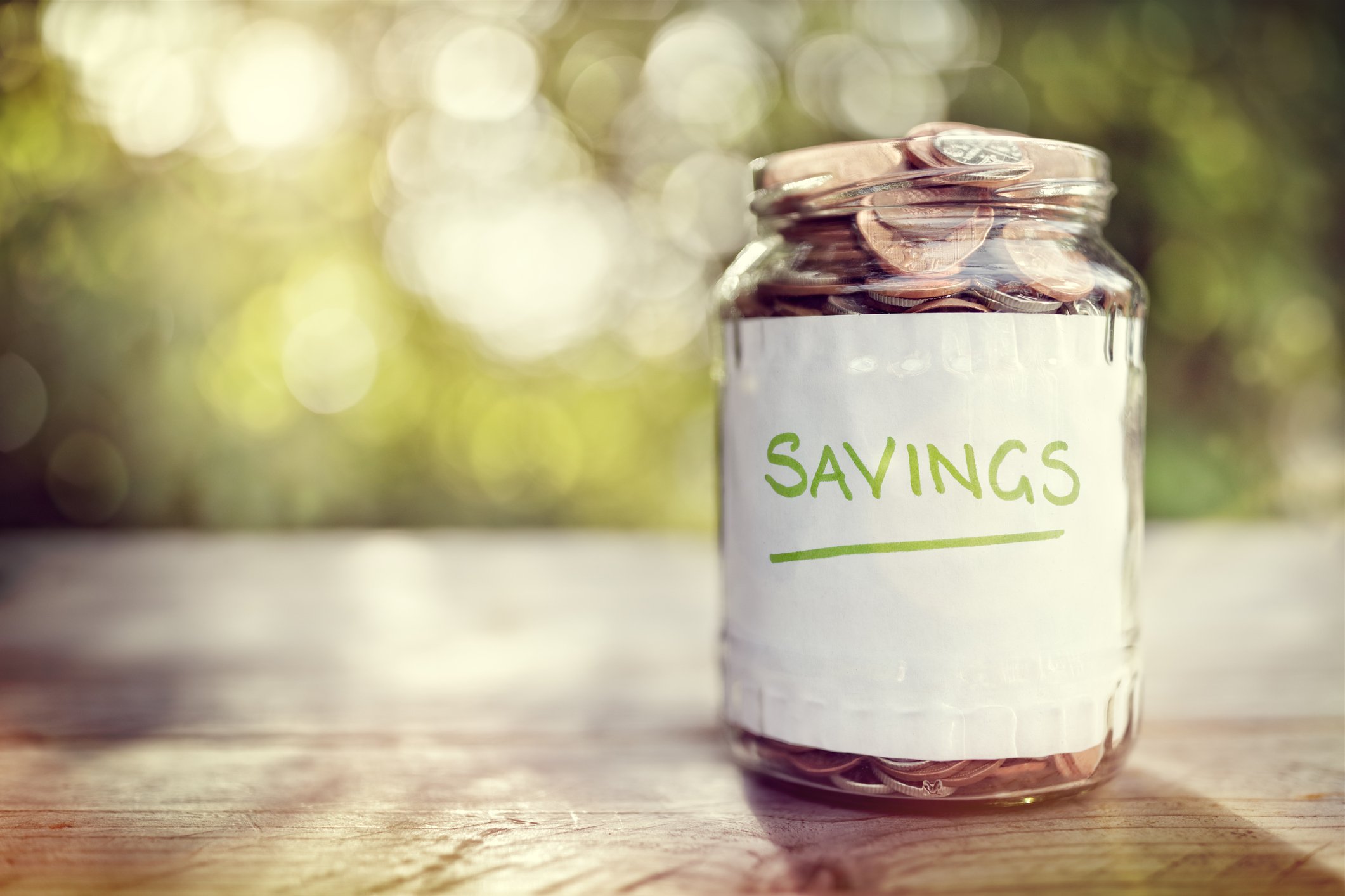 Jar of coins on a wooden surface labeled savings