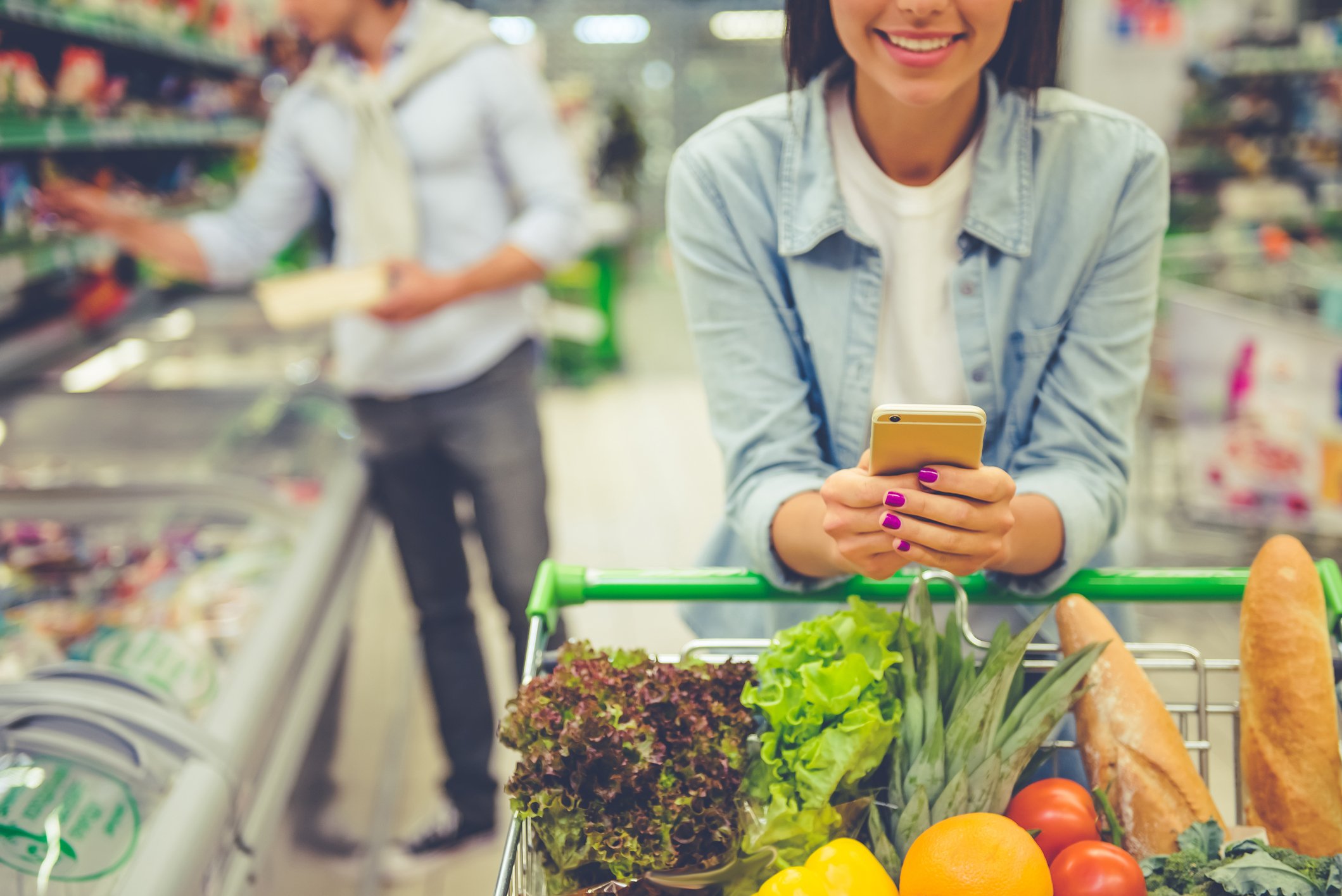 A young woman buys groceries and uses her smartphone