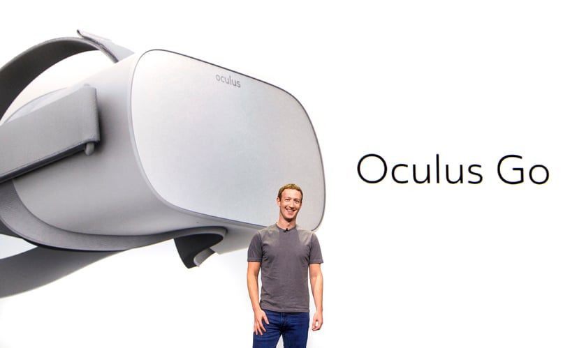 Mark Zuckerberg standing in front of a screen that has a VR headset on it.