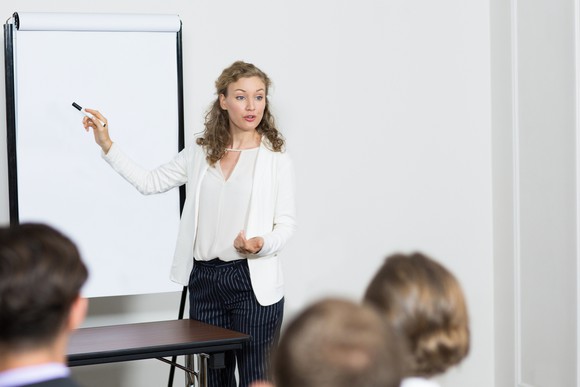 Professionally dressed female pointing to a white board in front of others