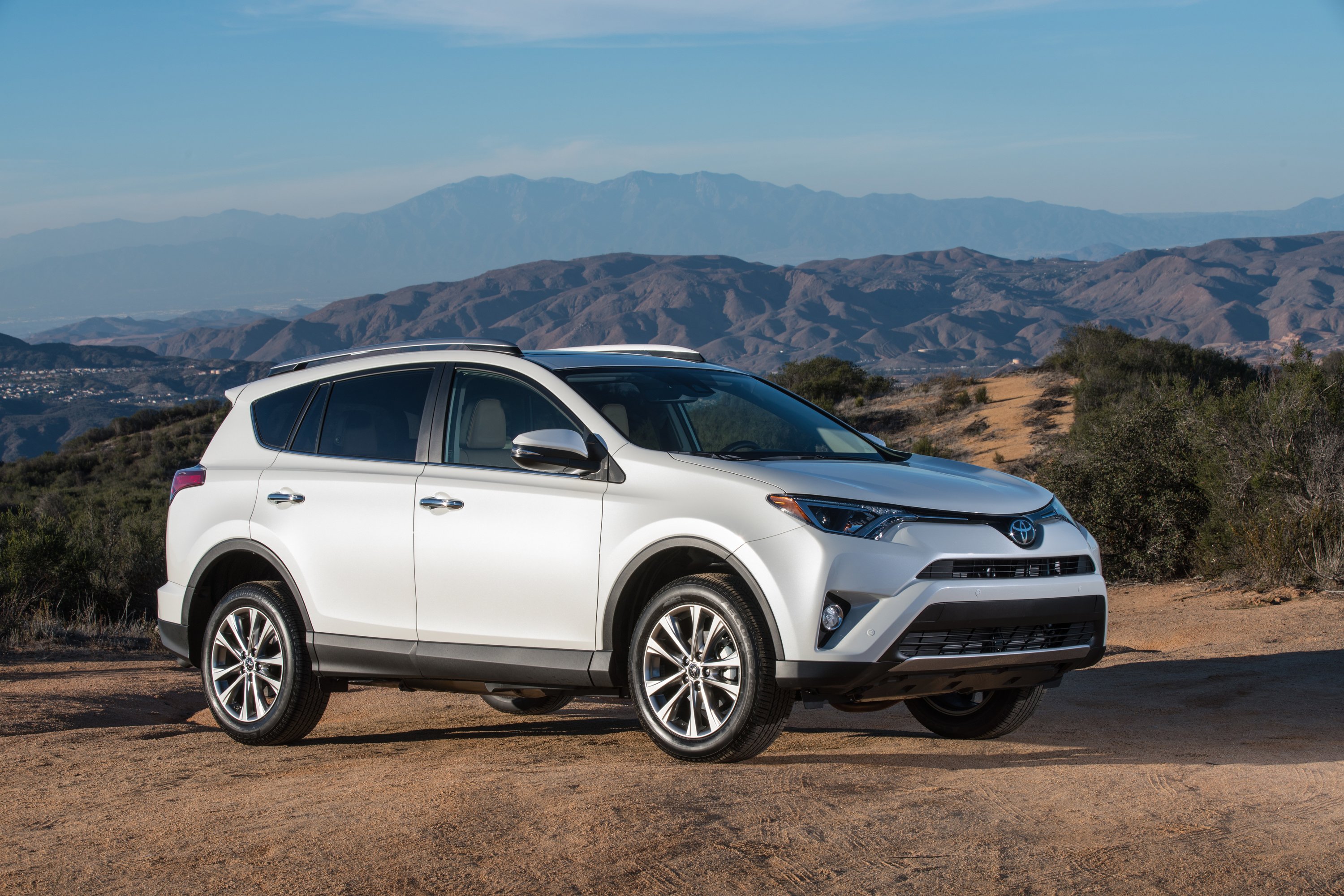 A silver Toyota RAV4 crossover SUV parked on dirt with mountains in the background.