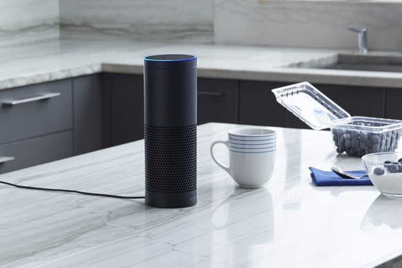 A black Amazon Echo placed on a kitchen counter near a coffee cup and blueberries.