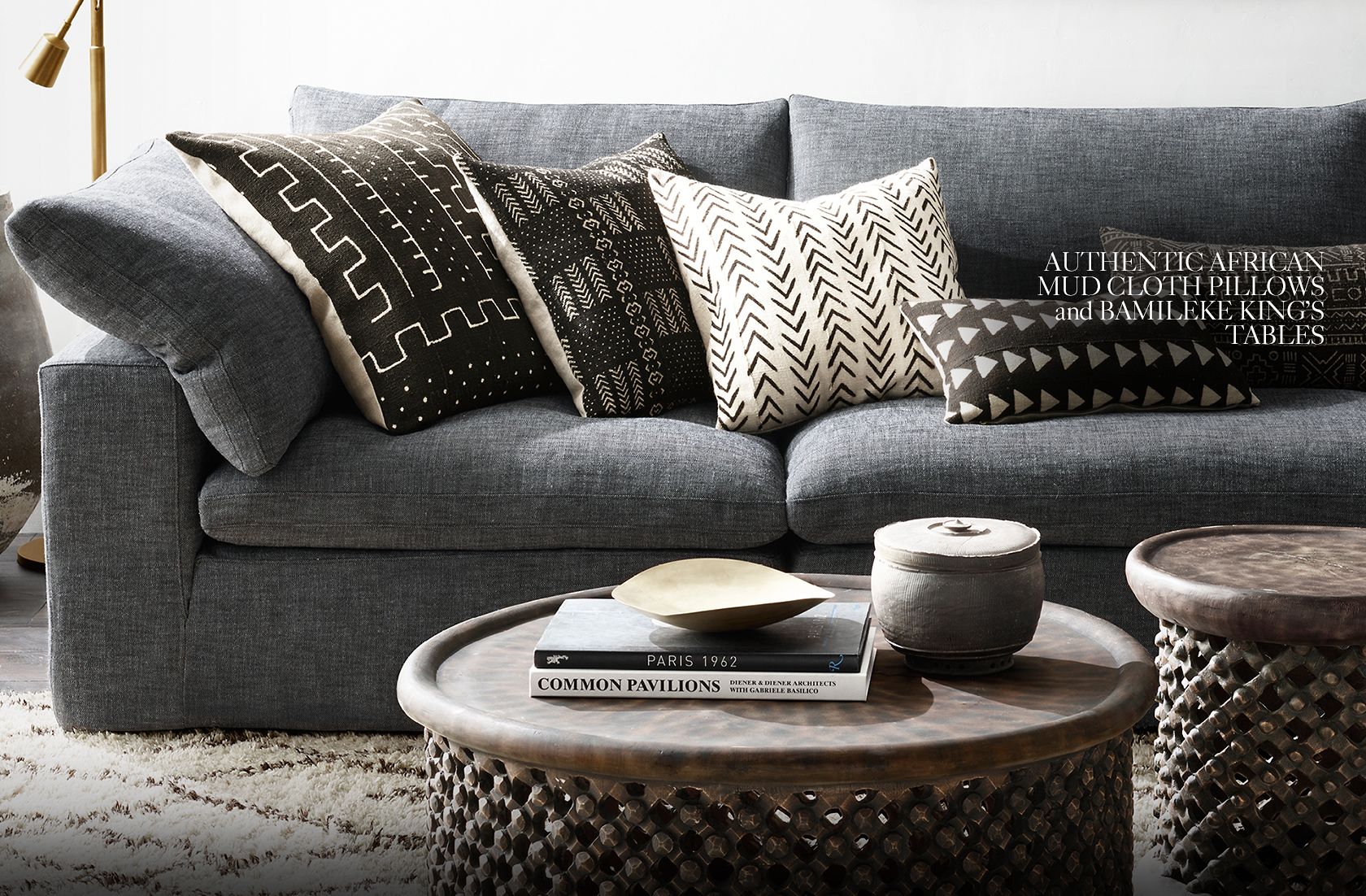 Gray couch with mud-colored pillows and decorative tables with a fuzzy rug and brass lamp.
