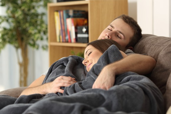 A young couple, snuggling and asleep on the couch.