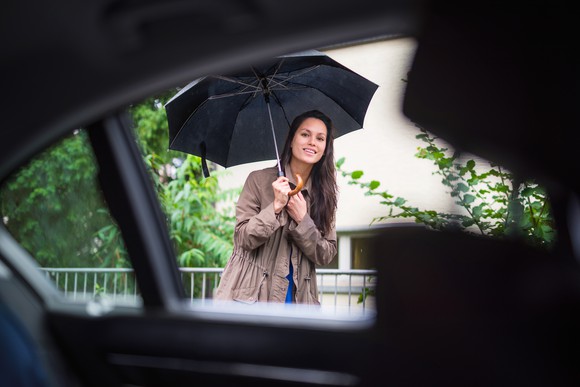 Woman holding a black umbrella peeks into the back of a car to check if it's her Uber ride