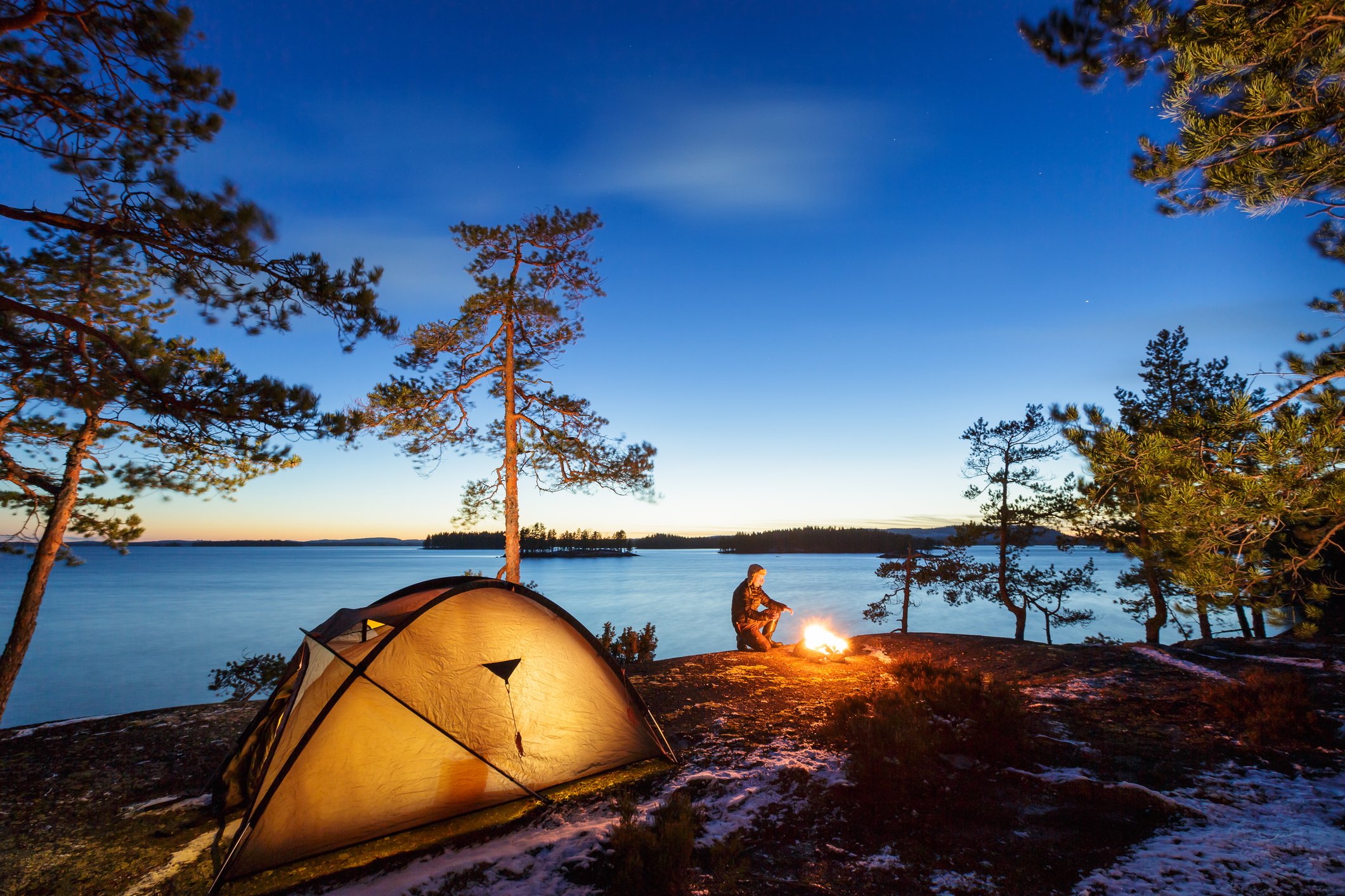 A camping tent and a man by a campfire by a lake