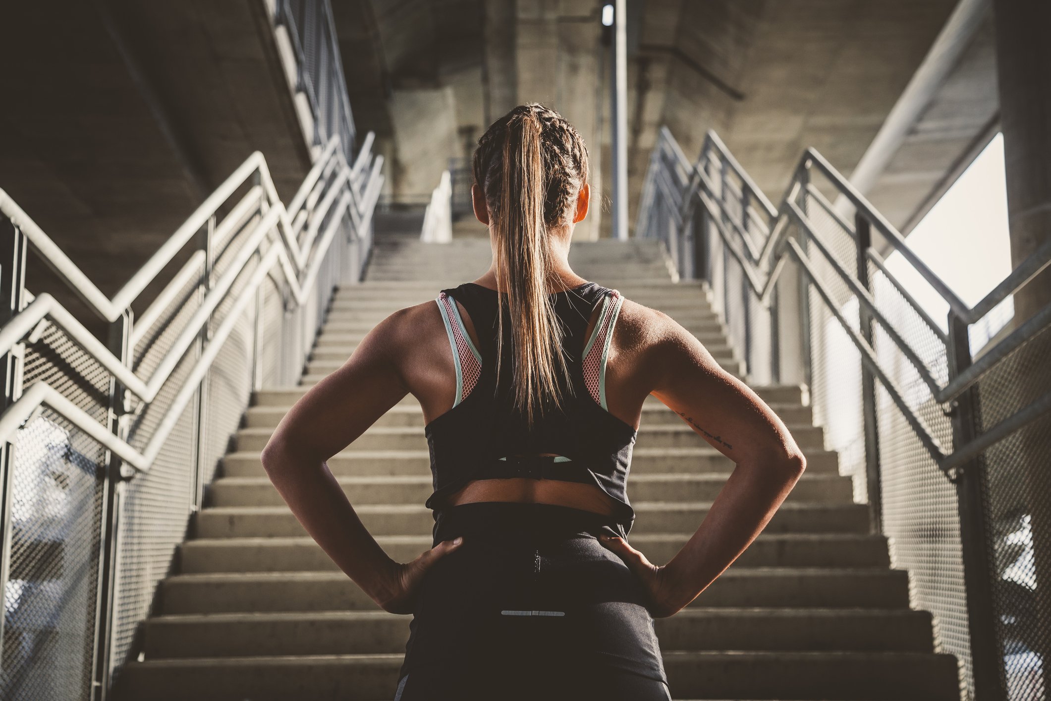 A woman dressed in athletic clothing stands at the bottom of a staircase.