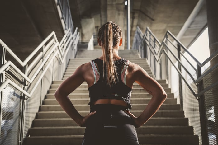 A woman dressed in athletic clothing stands at the bottom of a staircase.