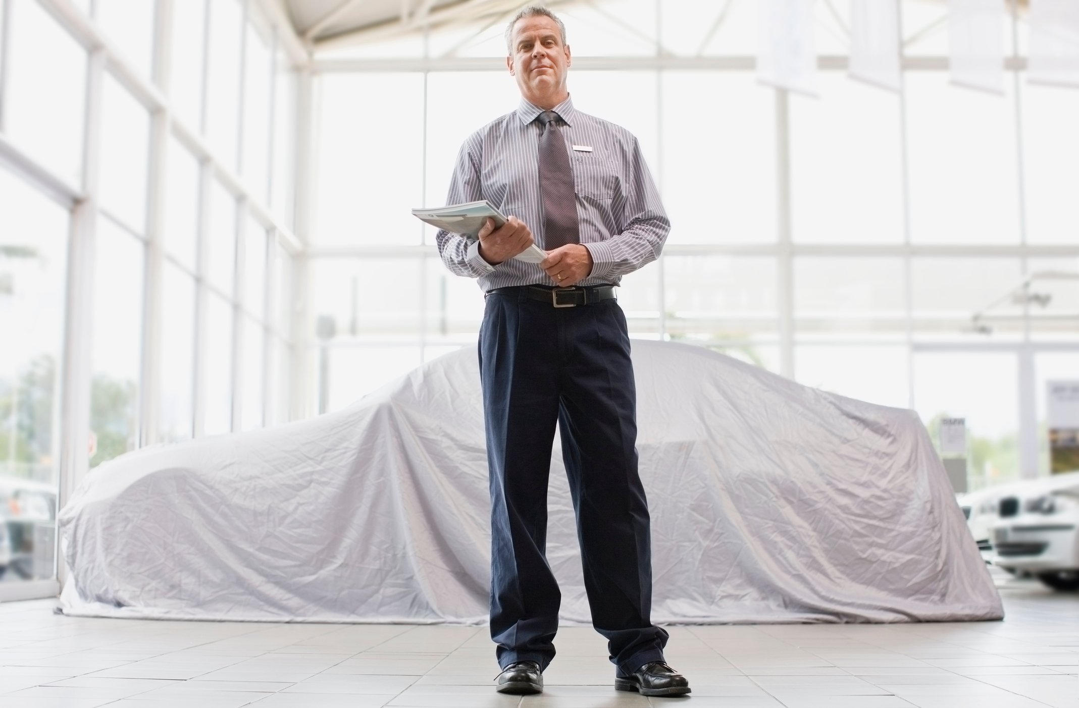 A salesman stands in front of a used car.
