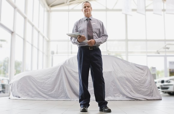 A salesman stands in front of a used car.