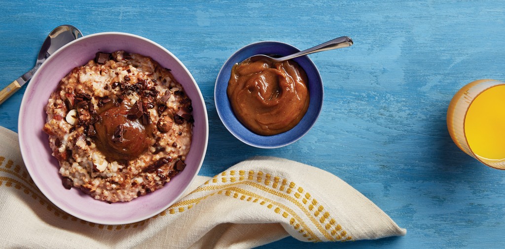 A bowl of pear butter next to a bowl of granola on a blue table.