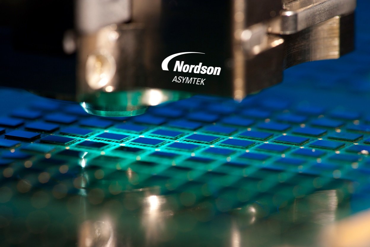 Piece of equipment labeled Nordson Asymtek helping to scan a row of semiconductor chips.
