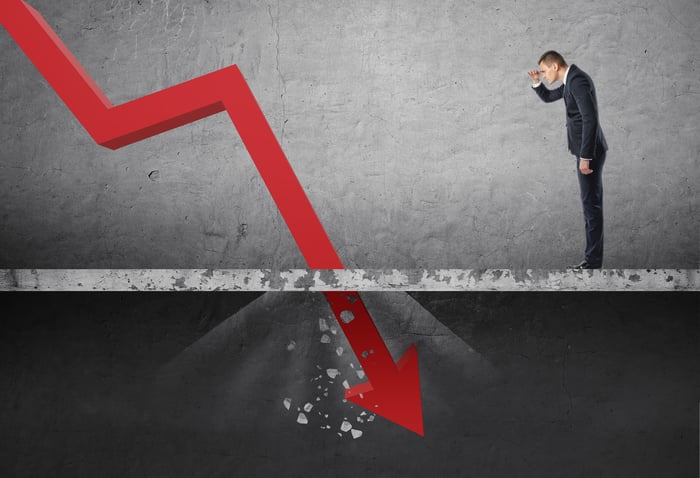 Businessman looking down at the falling red arrow destroying a concrete barrier.