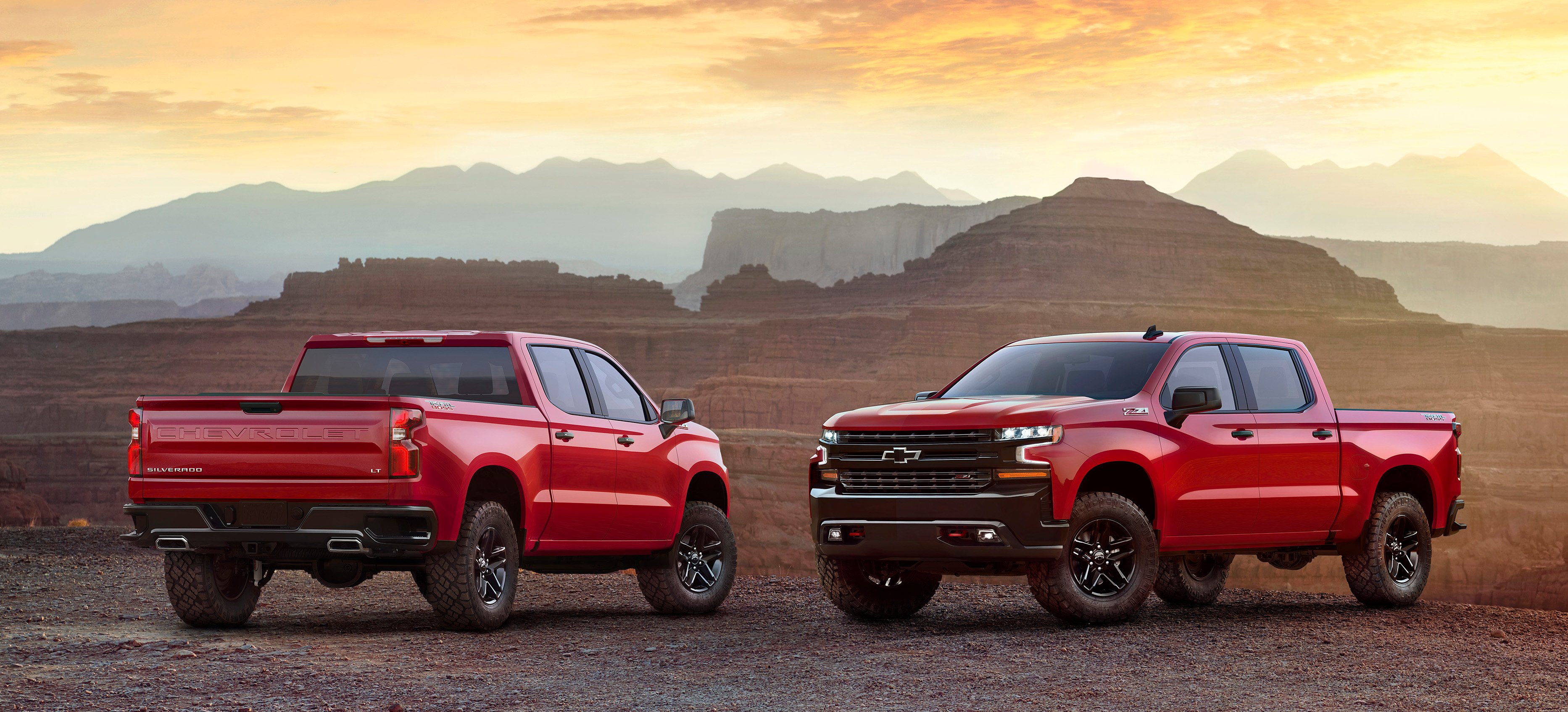 2 red 2019 Chevrolet Silverados, parked to display front and rear details, in a rugged desert setting.