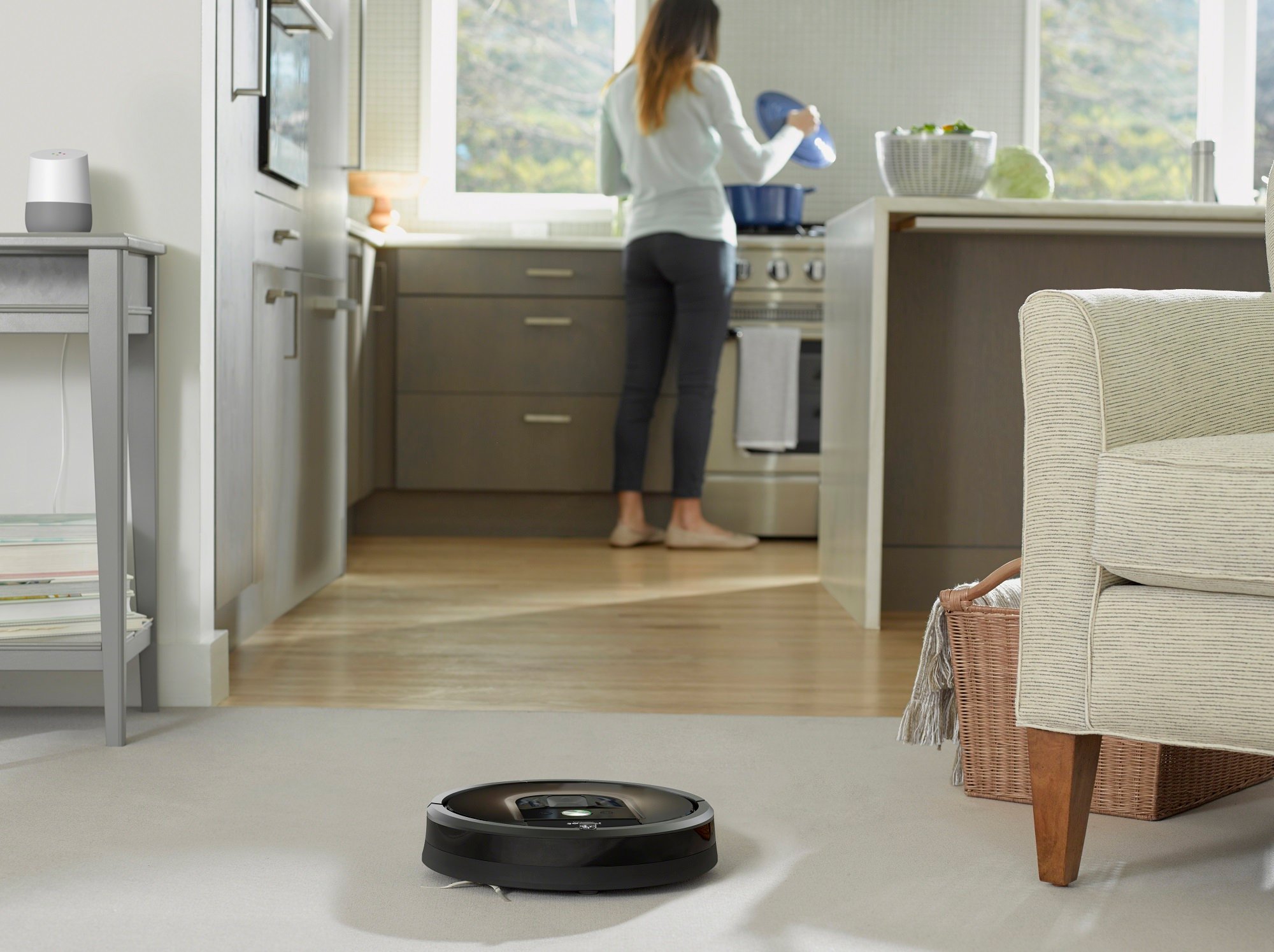 iRobot Roomba 980 vacuum cleaning the floor while a homeowner works in the kitchen