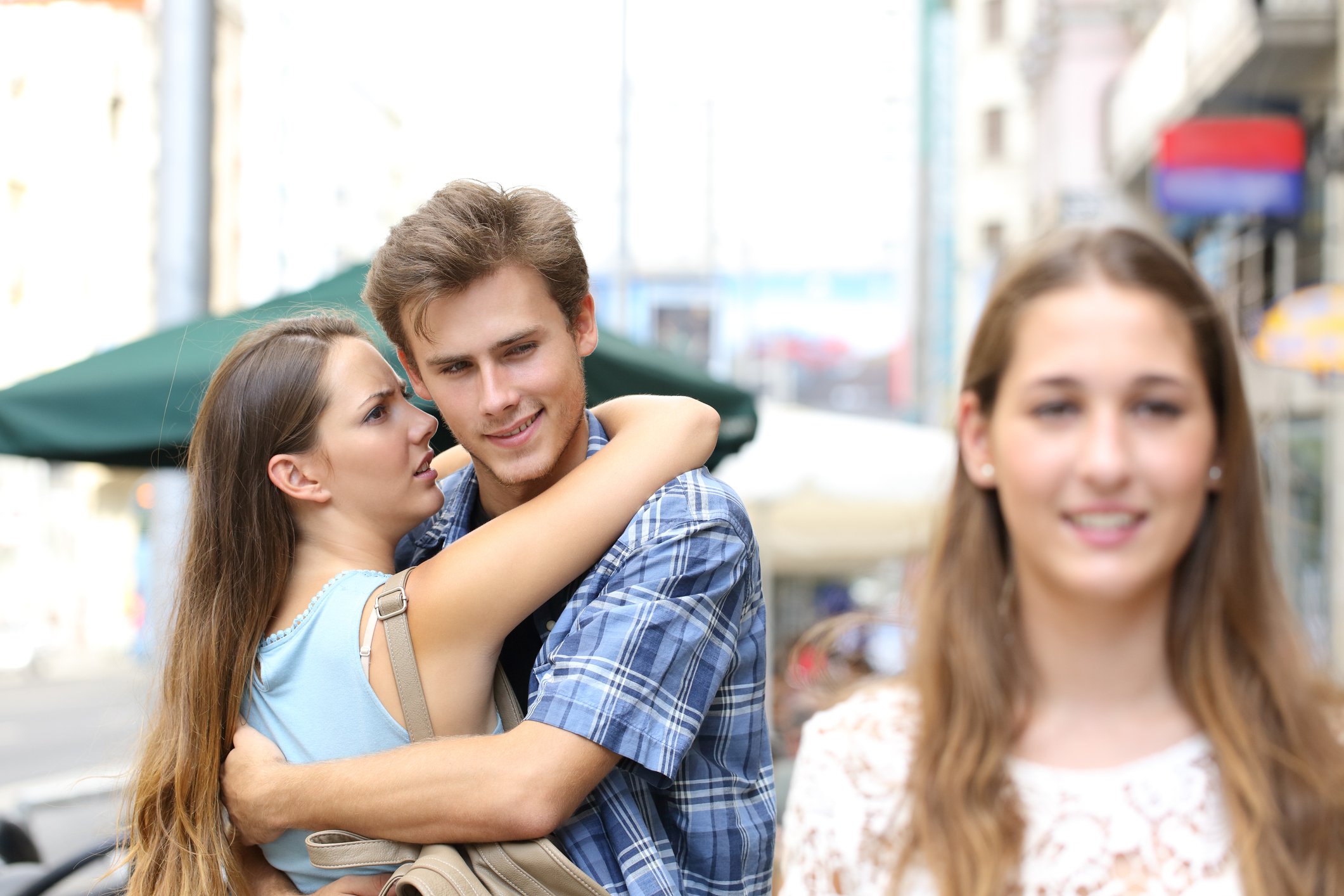 Young man gawks at a passing head-turned while hugging his current girlfriend.
