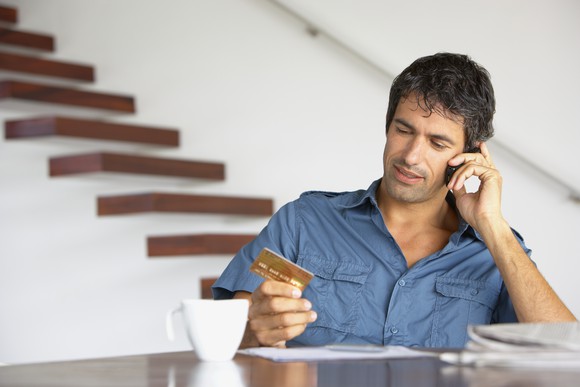 A man at a table on  the phone looking at his credit card. 