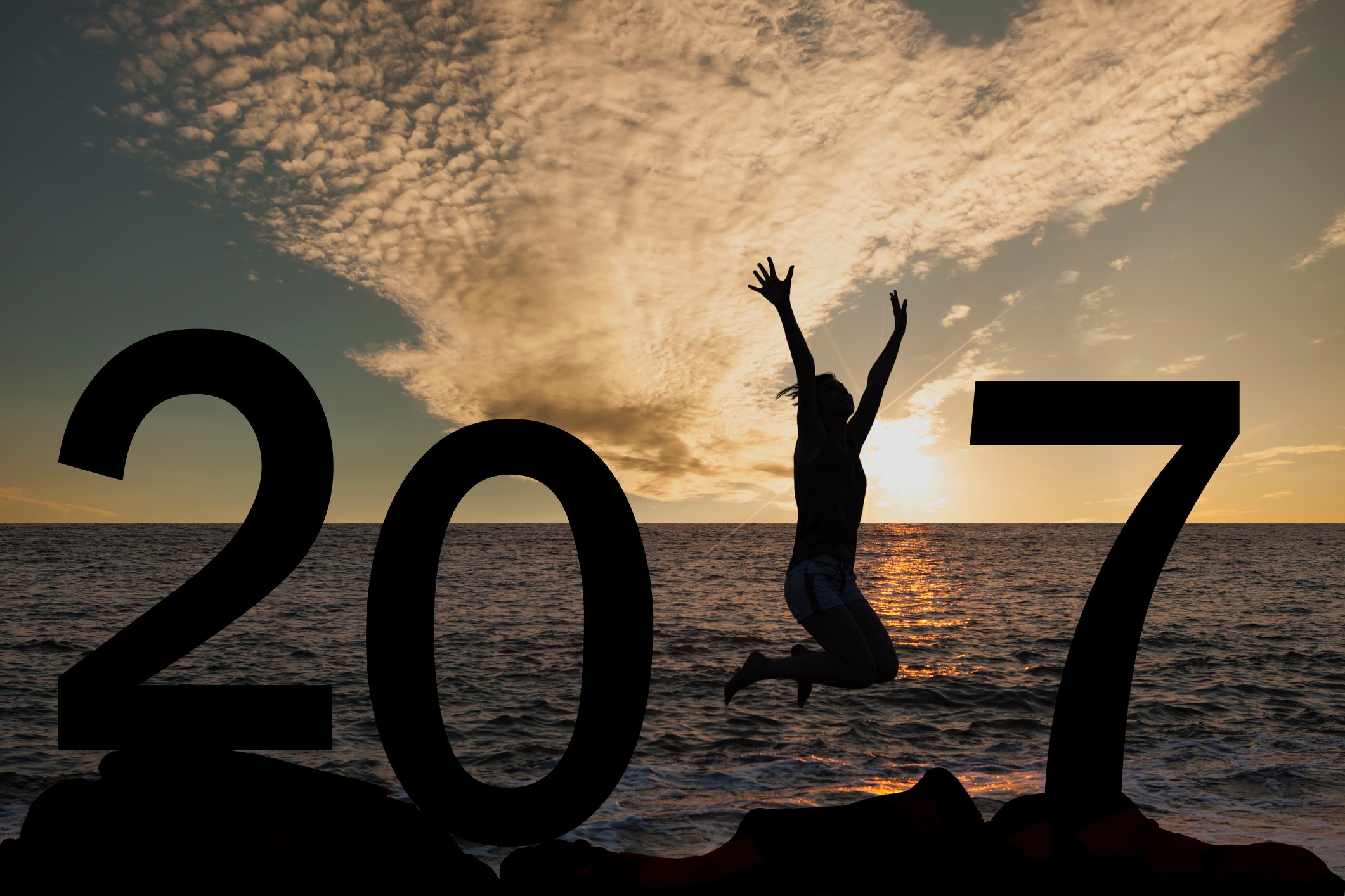 Silhouette of 2017 at sunset in front of ocean with woman jumping where the 1 would be