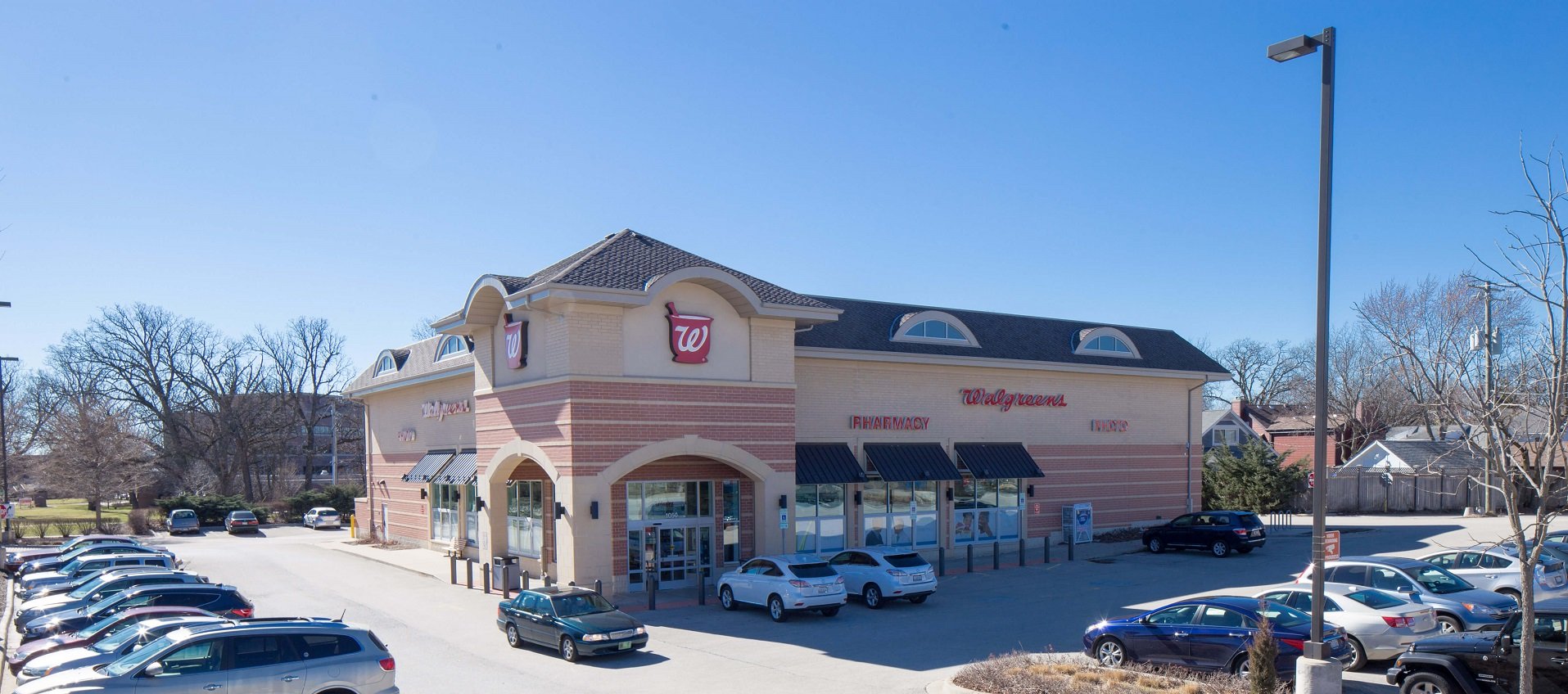 Walgreens store with full parking lot on a sunny day under blue sky.
