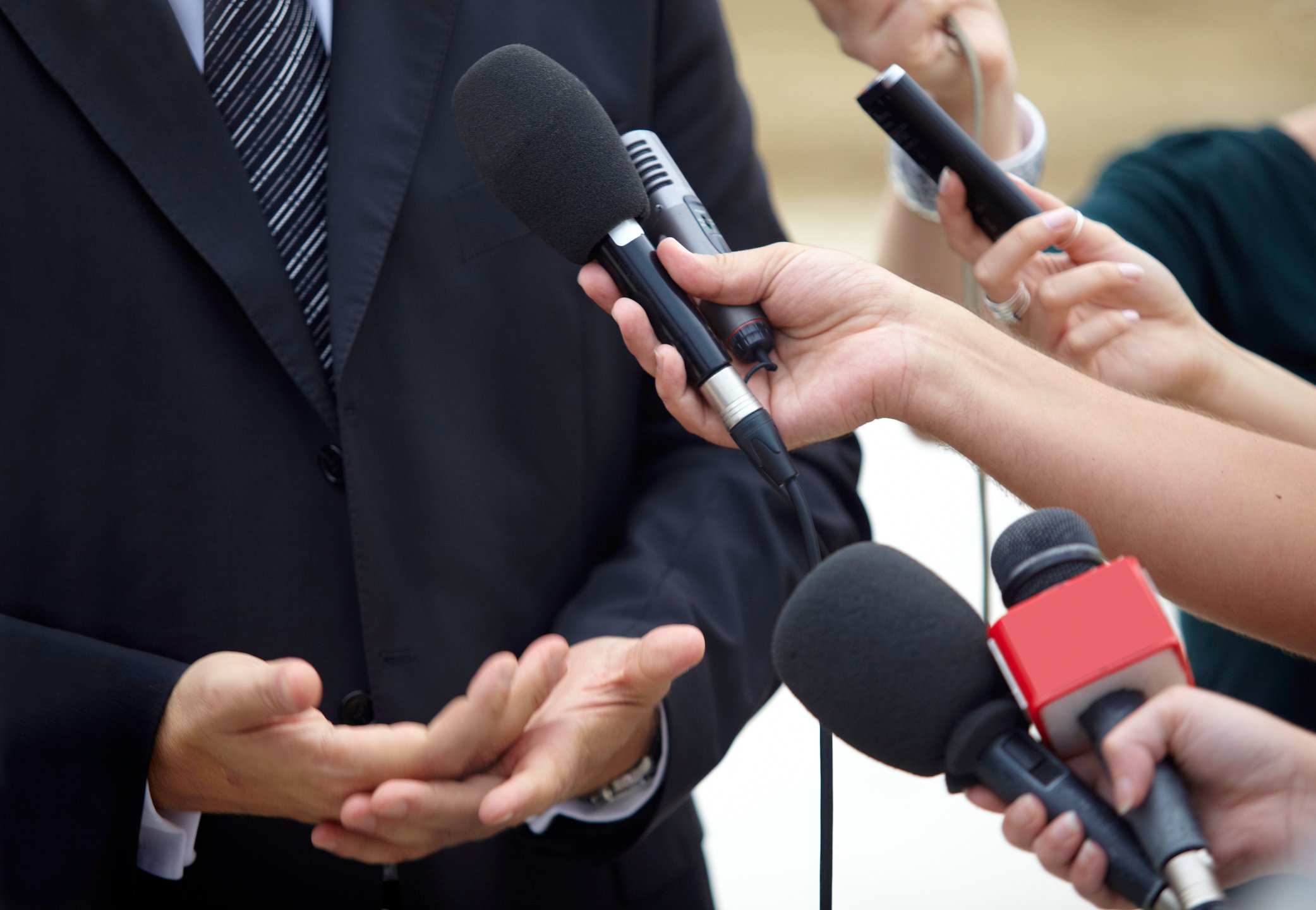 People pointing microphones at a man in a suit
