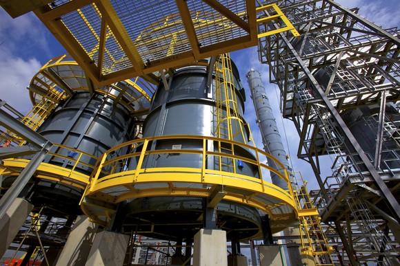 Close-up of refinery equipment, including tall grey storage tanks surrounded by yellow walkways.