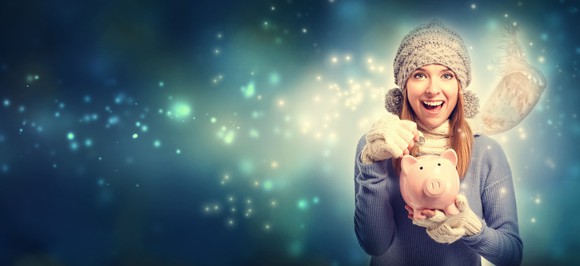 A young woman in a scarf puts coins into a piggy bank.